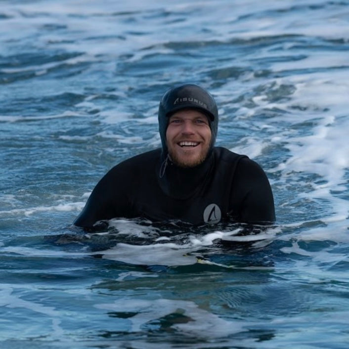Person in a wetsuit and helmet floating on a surfboard in the water