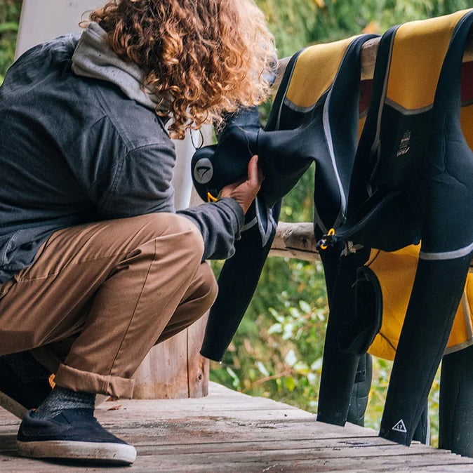 Person preparing a wetsuit on a wooden platform with greenery in the background